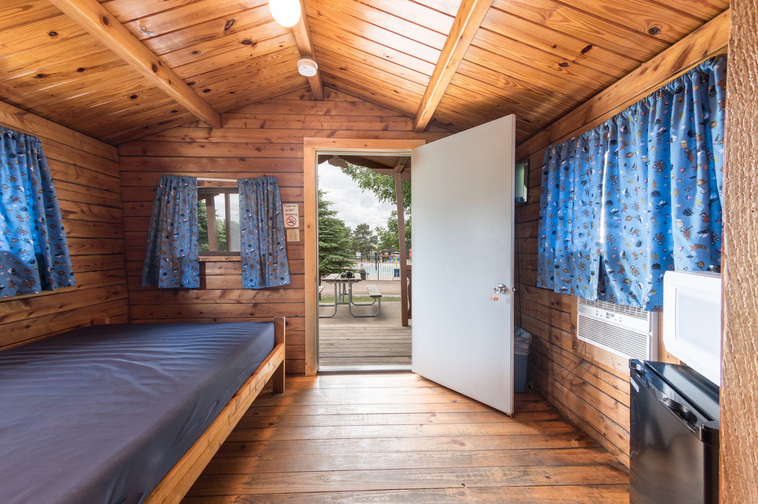 Interior of rustic cabin, front room with full size bed, refridgerator and microwave