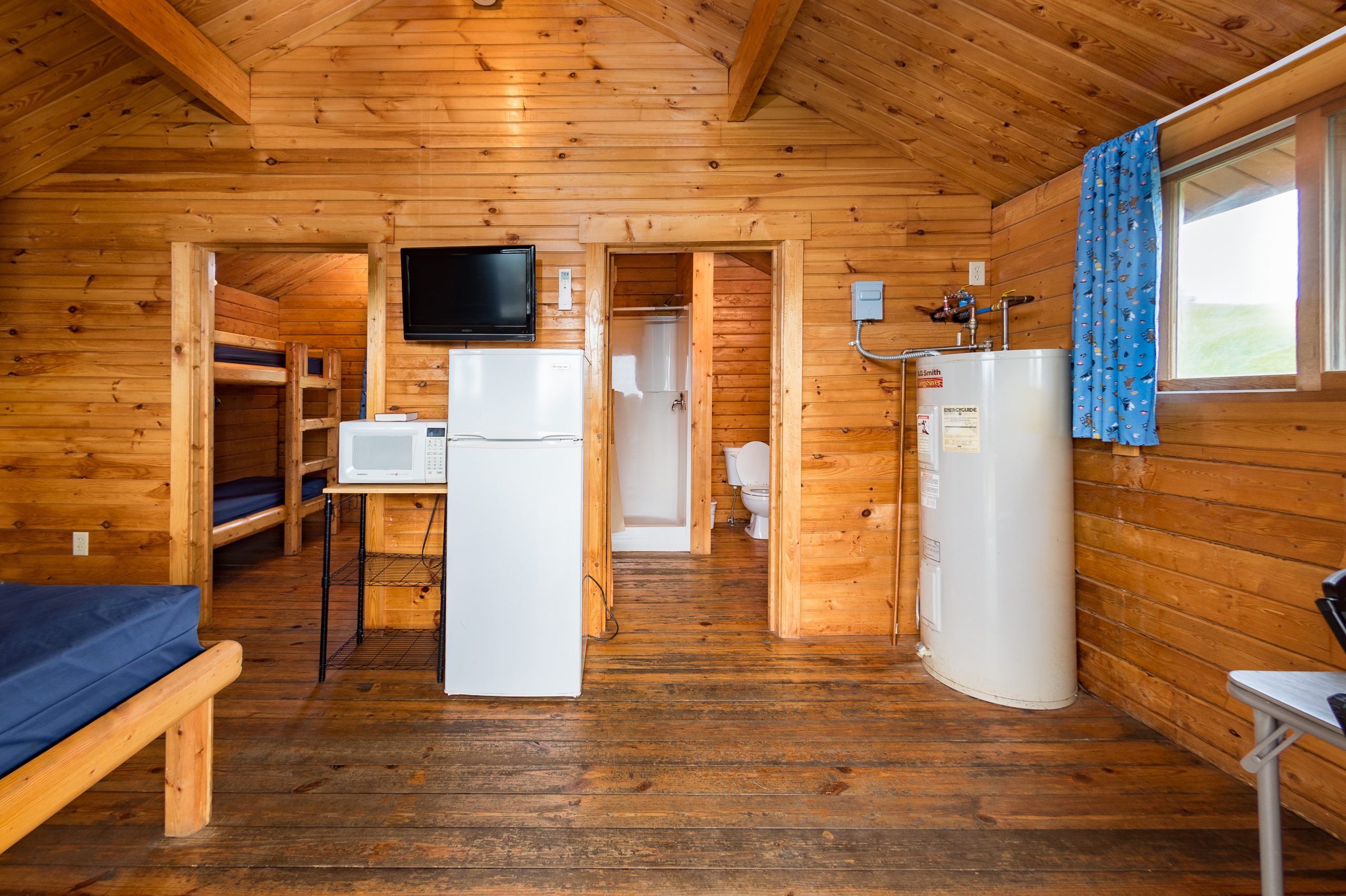 Front room of bungalow, full size bed, refridgerator, microwave, tv, and small table