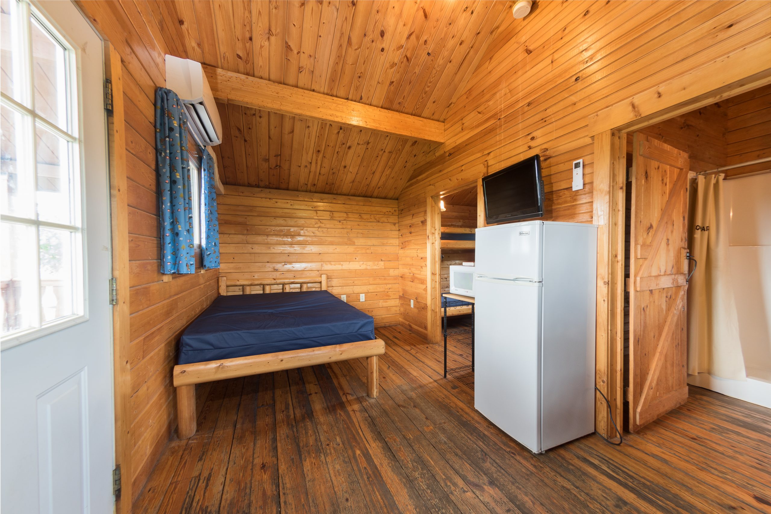 Front room of bungalow, full size bed, refridgerator, microwave, tv, and small table