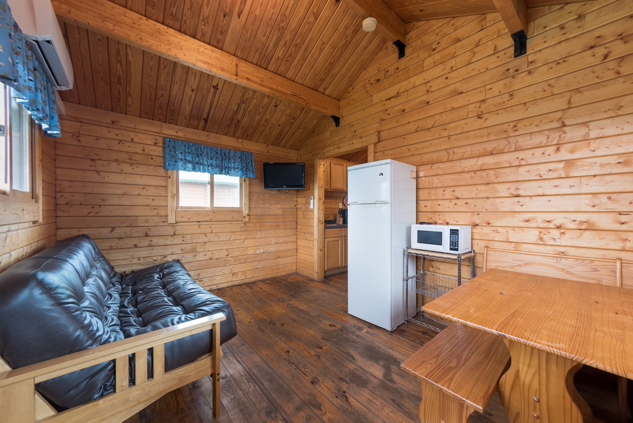 Front room of cottage including table, futon, refrigerator, microwave and tv