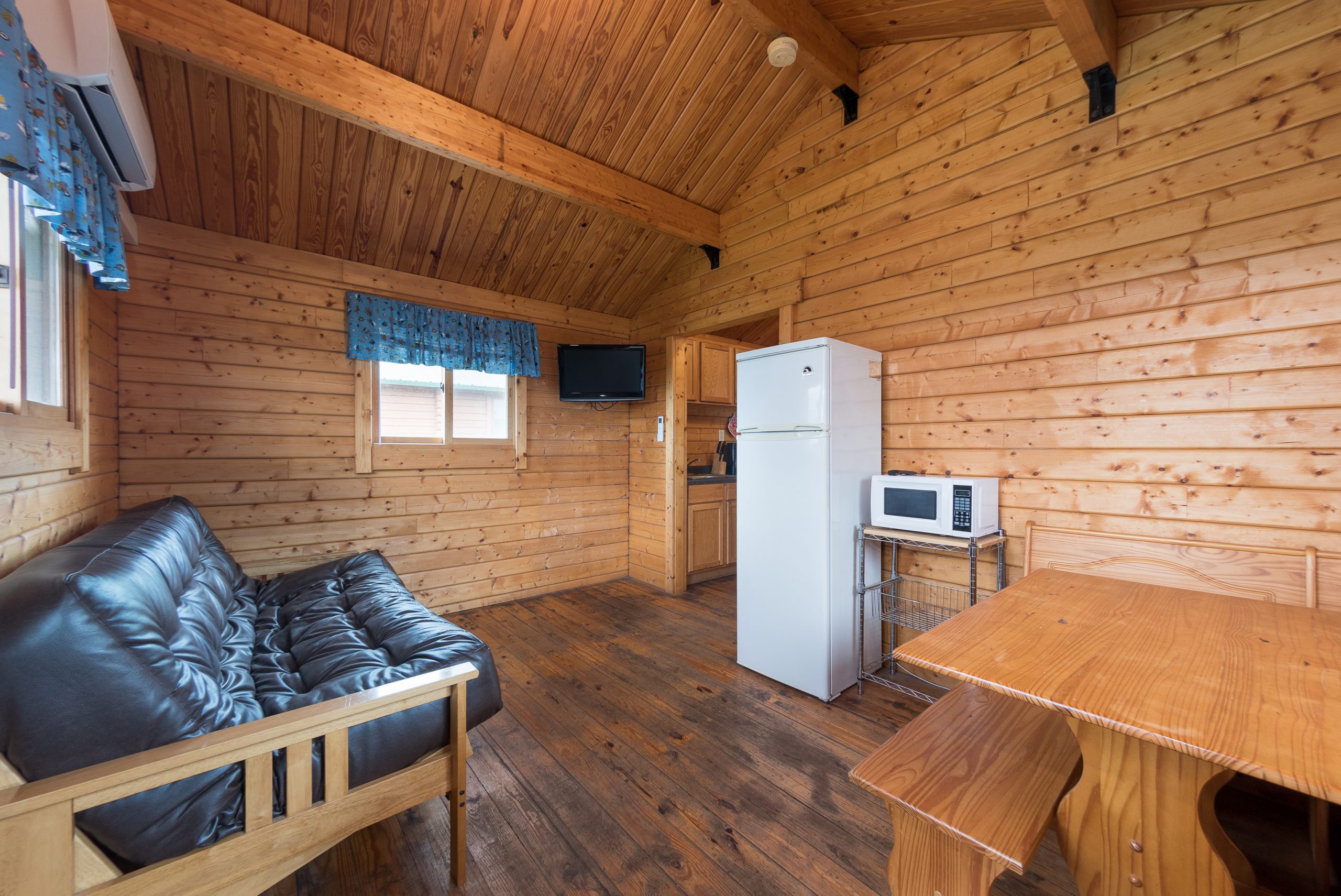 Front room of cottage including table, futon, refrigerator, microwave and tv