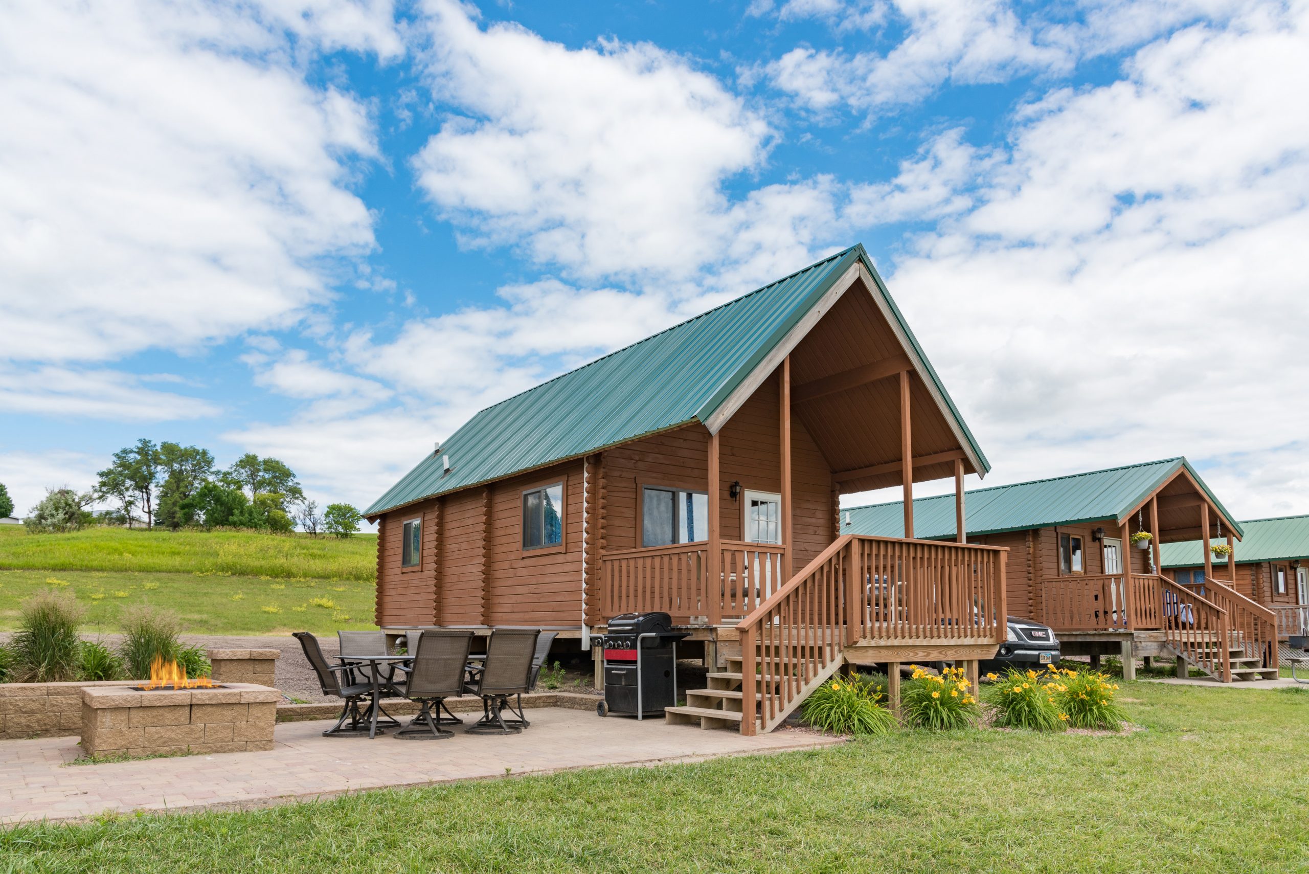 Front view of Ranger Retreat cabin, paver patio with fire pit, table and gas grill